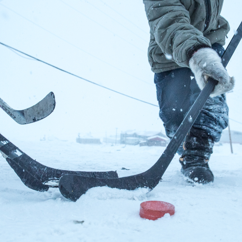 A closeup of a hockey puck amid three hockey sticks in the icy streets of Pond Inlet.