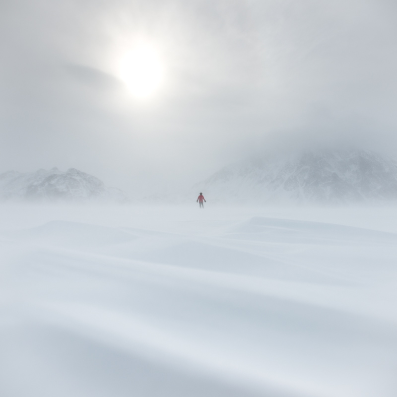A figure stands in the distance as snow rolls across a plain of sea ice.